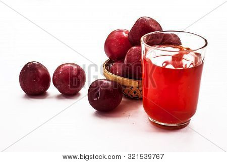 Raw Organic Red Ripe Plums In A Brown-colored Basket Along With Its Extracted Tincture Or Extracted