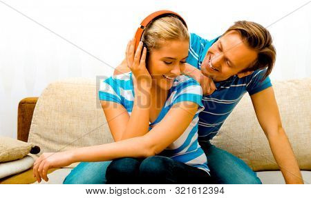 Young cuople having fun while sitting on sofa. Woman listening music in headphones.