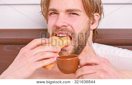French Breakfast Stereotype. Handsome Man Browsing Internet In Bed. Guy Having Coffee And Holds Croi
