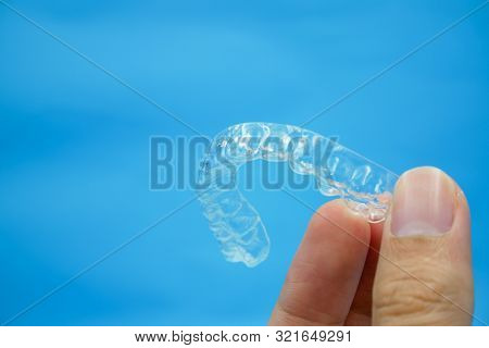 Hand Holding Clear Plastic Retainer Teeth That Isolated On Blue Sky Background. It's An Equipment Fo