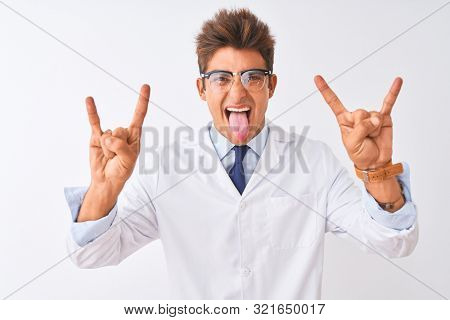 Young handsome sciencist man wearing glasses and coat over isolated white background shouting with crazy expression doing rock symbol with hands up. Music star. Heavy music concept.