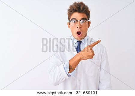Young handsome sciencist man wearing glasses and coat over isolated white background Surprised pointing with finger to the side, open mouth amazed expression.