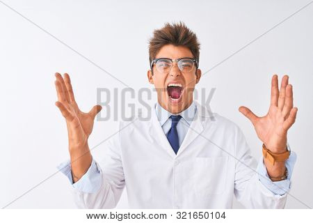 Young handsome sciencist man wearing glasses and coat over isolated white background crazy and mad shouting and yelling with aggressive expression and arms raised. Frustration concept.