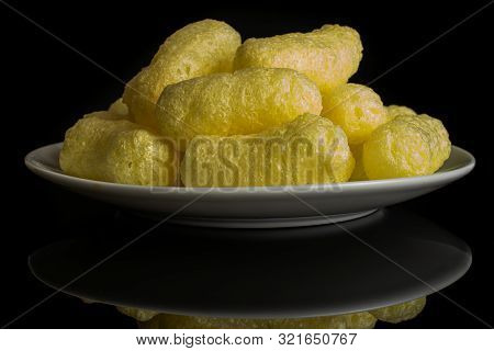 Lot Of Whole Salted Yellow Corn Puff On White Ceramic Plate Isolated On Black Glass