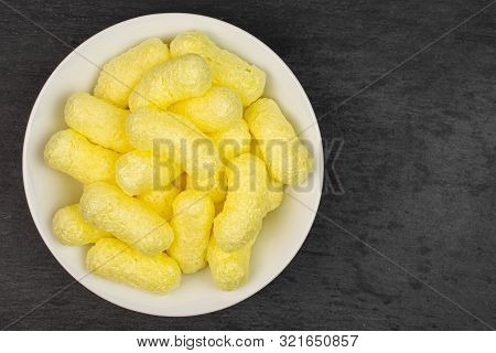 Lot Of Whole Salted Yellow Corn Puff On White Ceramic Plate Flatlay On Grey Stone