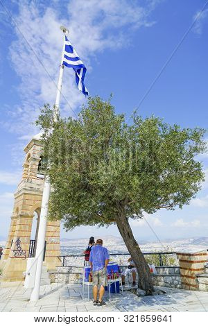 Athens Greece - July14 2019; Cold Drinks Vendor Under Olive Tree And Flagpole By Belltower At Summit