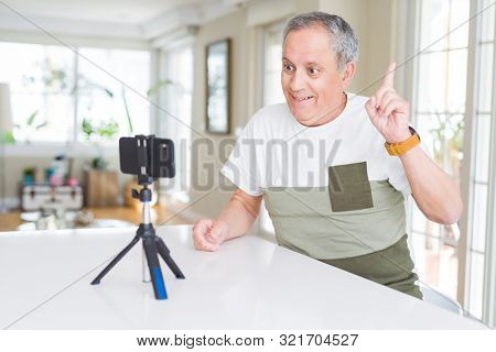 Handsome senior man doing video conference talking to the smartphone camera pointing finger up with successful idea. Exited and happy. Number one.