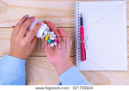 Top View Of Woman Hands Holding White Bottle Pill To Taking Medication With Book And Pen On Wooden T