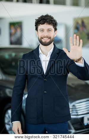 Young Man Saleman Of Car In Auto Showroom Greeting Client