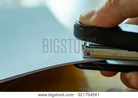 Woman's Right Hand Holding Stapler And Stapling White Paper On Wooden Background, Close Up & Macro S