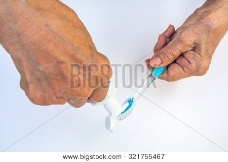 Senior Woman's Hands Squeezing Toothpaste On Brush Against Isolated On White Background