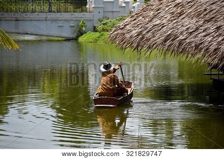 Kanchanaburi, Thailand, 09.09.2019: A Thai Man In Traditional Thai, Siamese Dress Is Rowing An Old T