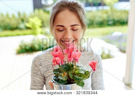 farming, gardening and people concept - happy young woman smelling pink cyclamen flowers in pot at summer garden