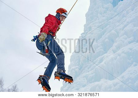 Alpinist Woman With Ice Tools Axe In Orange Helmet Climbing A Large Wall Of Ice. Outdoor Sports Port