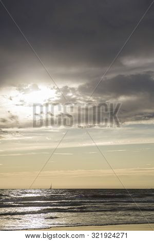 Vertical Photo Of A Sunset At La Barrosa Beach In Sancti Petri, Cadiz, With Sailboat Sailing By The 