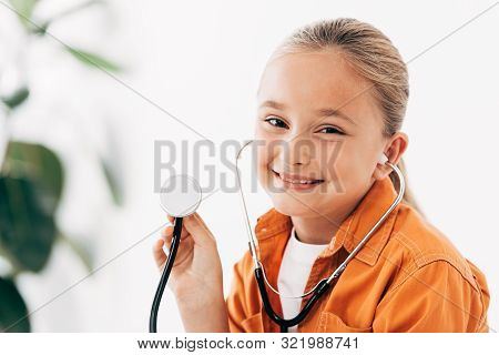 Smiling Child Holding Stethscope And Looking At Camera In Clinic
