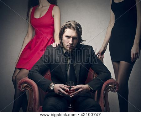 smuk mand sidder på stolen med to smukke kvinder bag