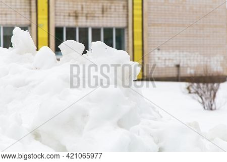 A Large White Snowdrift Piled On A City Street Against The Backdrop Of A House. A Block Of Snow With