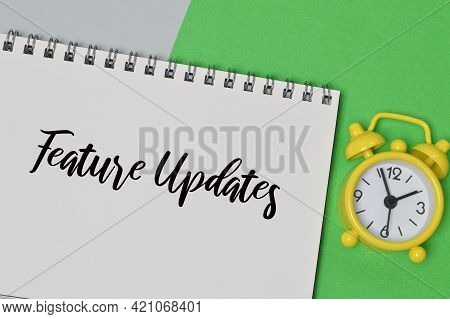 Top View Of Clock And Notebook Written With Feature Updates.