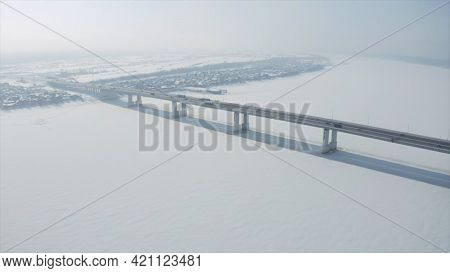 Aerial View Of A Long Bridge Above Snow And Ice Covered River Between Two Parts Of A City. Clip. Win