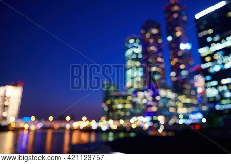 Night Bokeh Light In Big City. Defocused Illuminated Skyscrappers And River Of City Downtown. Abstra