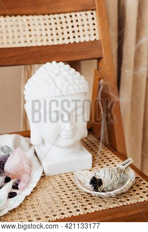 Buddha head statue by a burning sage smudge cleansing the house