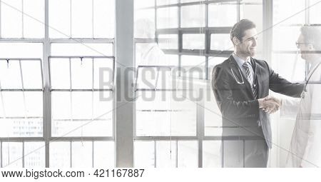 Composition of two smiling male doctors shaking hands in corridor with double exposure. healthcare, partnership and success concept digitally generated image.