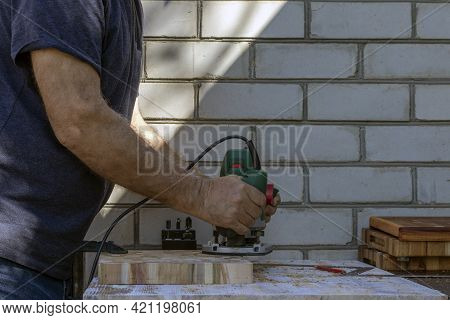 A Carpenter At A Hand-held Hand-held Milling Machine In A Carpentry Workshop. End Cutting Boards. Jo