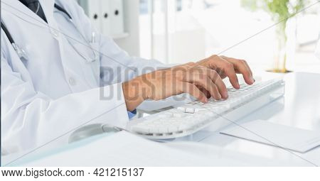 Mid section of caucasian male doctor typing on keyboard at hospital. healthcare and medical professionalism concept