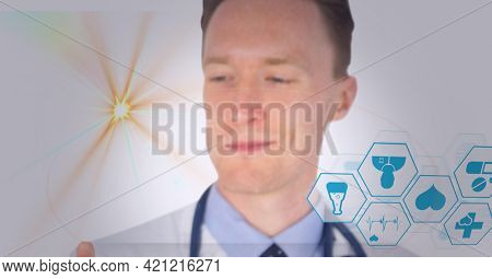Spot of light and multiple medical icons over caucasian male doctor against white background. healthcare and medical professionalism concept