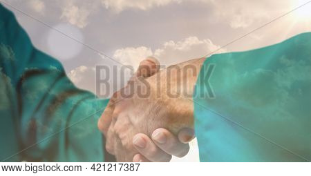 Digital composite image of mid section of surgeons shaking hands against clouds in the sky. global finance and healthcare concept