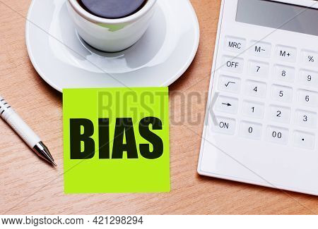 The Wooden Table Has A White Cup Of Coffee, A Pen, A White Calculator, And A Green Sticker With The 