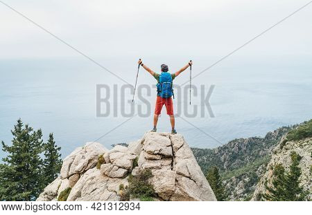 Young Hiker Backpacker Man Rose Trekking Poles Up Enjoying The Mediterranean Sea On Clifftop During 