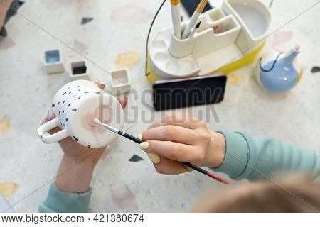 Women's Hands Paint A Pink Heart On The Back Of A Ceramic Cup With A Brush. Training In The Professi