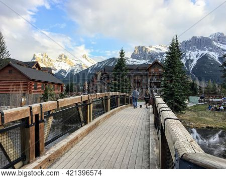 Canmore, Alberta, Canada - May 14th, 2021: A Couple Going For An Evening Walk Across A Bridge Surrou