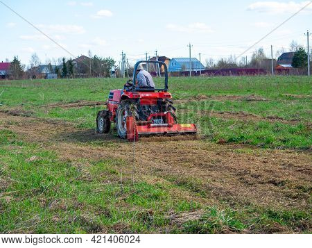 A Man Rides A Tractor With A Mower In A Field. Mulching And Mowing The Grass. Clear Day, Blue Sky. L