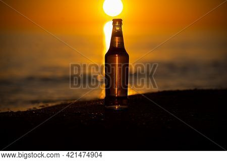 An Ice Cold Beer / Soda Bottle Standing Straight On The Golden Sands At Sunset. Summer Evening