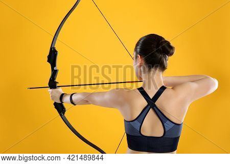Woman With Bow And Arrow Practicing Archery On Yellow Background, Back View