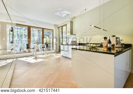 Big Panoramic Windows In Light Kitchen With White Cabinets And Black Counter Under Shiny Lamps