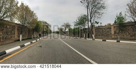 The Road Goes Off Into The Distance. An Empty Two-lane Highway Runs Between Stone Fences. One Car Is