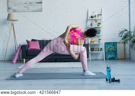 Back View Of Young Woman Working Out In Bound Side Angle Pose At Home.