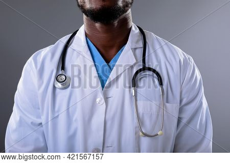 Mid section of african american male doctor wearing stethoscope against grey background. healthcare and medical professionalism concept
