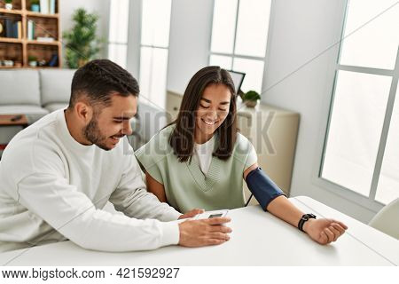 Young latin couple smiling happy measuring blood pressure using tensiometer at home.