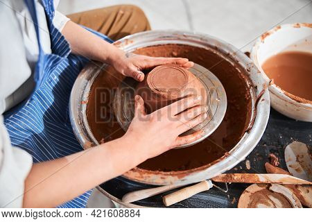 Adult Shaping Greenware Into Bowl With Hands On Potter Wheel