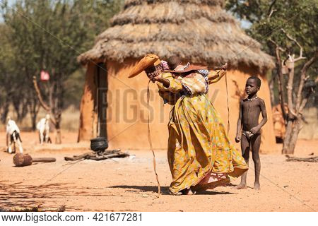 OPUWO, OTJIWARONGO REGION NAMIBIA - MAY 4, 2021: Young unidentified Himba woman with the typical dresses and hat in Himba living museum during a appearance in front of tourists