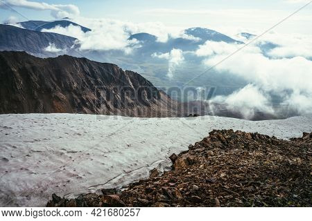View From Precipice Edge With Sharp Rocks And Snow Cornice To Mountain Valley In Low Clouds. Wonderf
