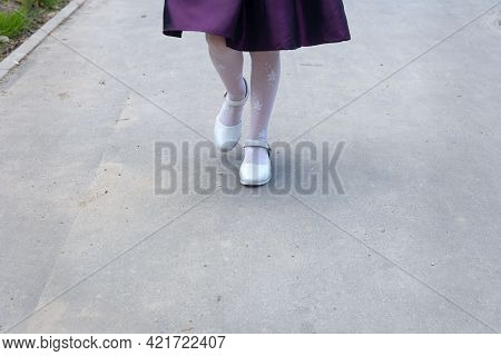 The Legs Of A Girl Of Six Years In Beautiful White Tights And And Elegant White Shoes. The Child Is 