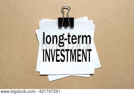 Long-term Investment. The Paper Is Clamped With A Clerical Clip. Paper On Wood Background.