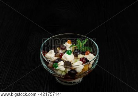 Salad from grapes apples pears kiwi oranges with mascarpone chease and cream. Healthy fresh fruit summer salad in glass bowl on black wooden background with copy space.