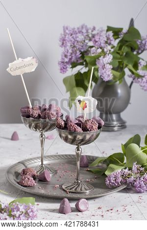 Belgian Sweets Cuberdon And Pralines In Silver Glasses, Spring Still Life With Lilac Flowers And Fla